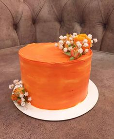 an orange frosted cake with flowers on top sitting on a table next to a couch