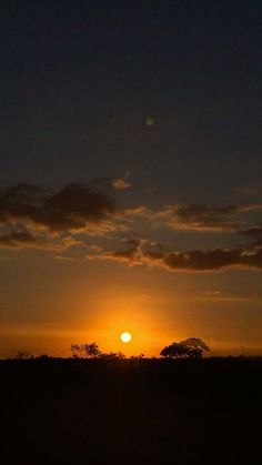 the sun is setting behind some clouds in the sky over an open field with trees