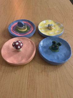 four plates with different designs on them sitting on a wooden table, one has a mushroom in the middle