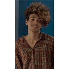 a young man with curly hair smiling at the camera while standing in front of a blue wall