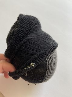 a hand is holding the top of a knitted black beanie hat with holes in it