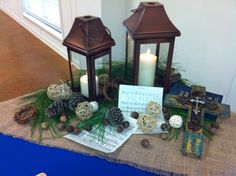 a table topped with two lanterns and pine cones on top of a cloth covered table