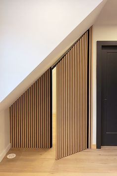 an empty room with wooden slats on the walls and floor, next to a black door