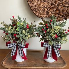 two white vases with red bows and greenery are sitting on a wooden table