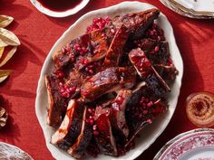 a white plate topped with ribs covered in pomegranate next to plates of food