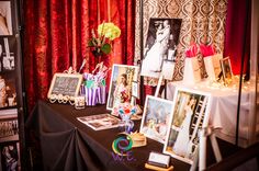 a black table topped with pictures and other items next to a red curtained wall