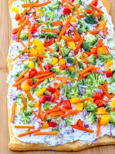 a pizza with vegetables on it sitting on top of a wooden table