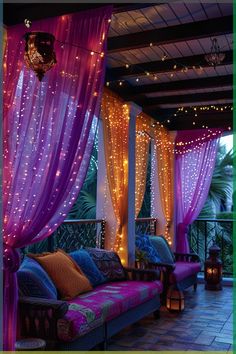 an outdoor living area with purple curtains and lights on the ceiling, couches covered in pillows