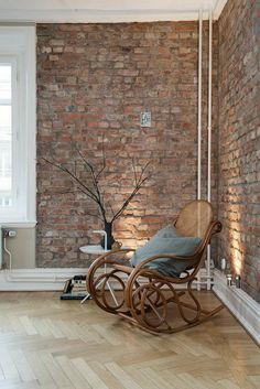 a wooden rocking chair sitting on top of a hard wood floor next to a brick wall