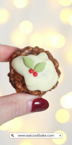 a hand holding a small pastry with icing and holly on it's face