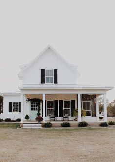 a large white house with black shutters on the front and side windows, sitting in an open field