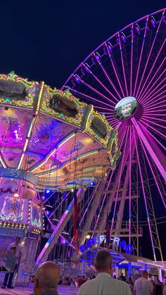 a ferris wheel lit up at night with people standing around