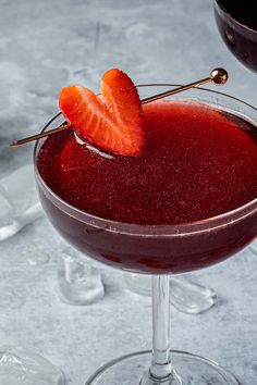 a close up of a drink in a glass with a strawberry on the rim and ice behind it