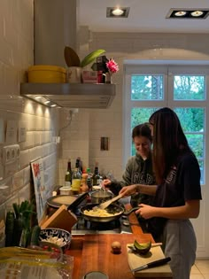 two people in a kitchen preparing food on top of a wooden counter next to a window