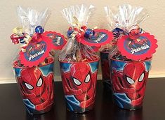 three plastic cups with spiderman candy wrapped in cellophane and tied to them