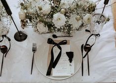 the table is set with white flowers and black utensils for an elegant dinner