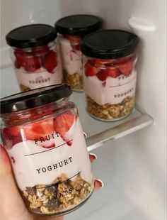 a person holding a jar filled with yogurt and strawberries