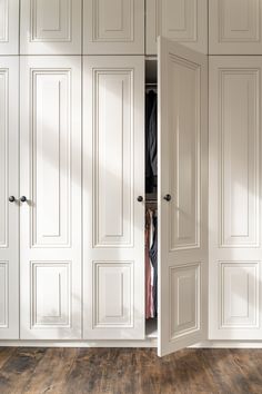 an open white closet door with clothes hanging on hangers and wooden flooring in front of it