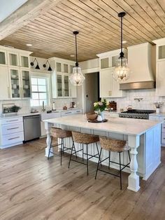 a large kitchen with white cabinets and wooden flooring on the ceiling, along with two bar stools in front of an island