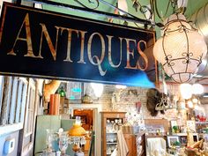 an antique store sign hanging from the side of a building with lots of antiques on display