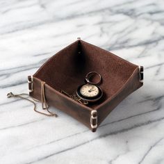 a small leather box with a pocket watch in it on a marble countertop top