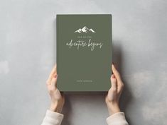 a person holding up a book with mountains in the background