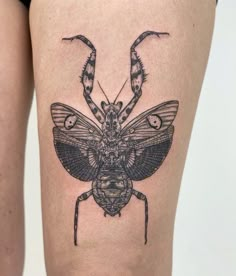 a black and white photo of a bug tattoo on the thigh, it looks like an insect