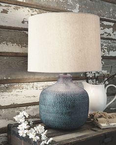 a blue vase sitting on top of a wooden table next to a white jug and lamp