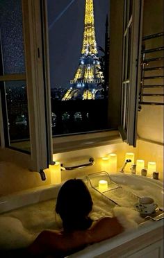 a woman in a bathtub with the eiffel tower lit up at night