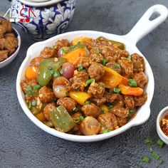 a white bowl filled with meat and vegetables next to two small bowls of chili sauce