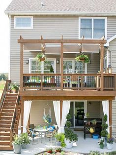 a deck with curtains on it and some potted plants in the back yard area