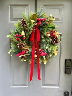 a christmas wreath with pine cones and red ribbon hanging on a door