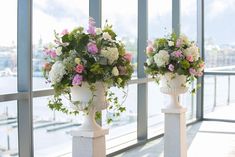 two white vases filled with flowers sitting next to each other on top of pillars