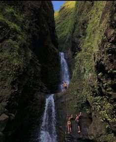 two people are climbing up the side of a waterfall while another person is standing in the water