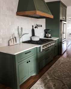 a kitchen with green cabinets and white tile backsplash, an oven hood over the stove