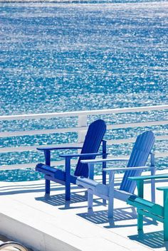 two blue and one green chairs sitting on a pier next to the ocean with water in the background