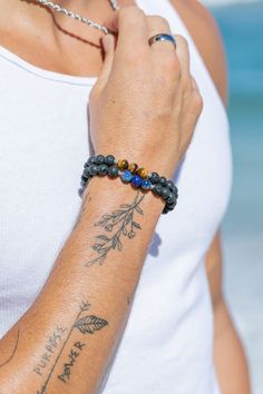 a woman wearing a white tank top holding onto a black beaded bracelet on her arm