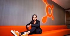 a woman sitting on top of an orange couch in front of a wall with the k logo