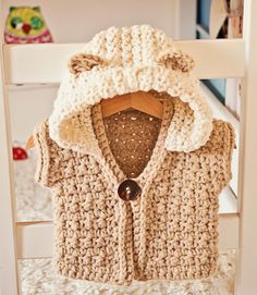 a crocheted sweater hanging on a wooden chair with a button in the middle