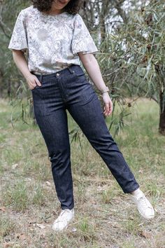 a woman standing in the grass with her hands on her hips, wearing jeans and a t - shirt