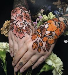 two hands with tattoos and flowers on their palms, one is holding the other's hand