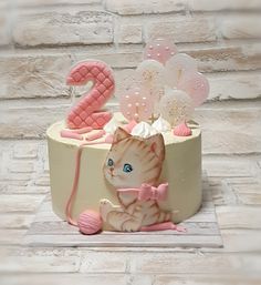 a birthday cake with a cat and number two on it's side, decorated in pink and white icing