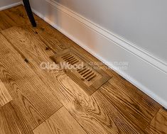 a wooden floor with a drain grate on the side and a white wall in the background