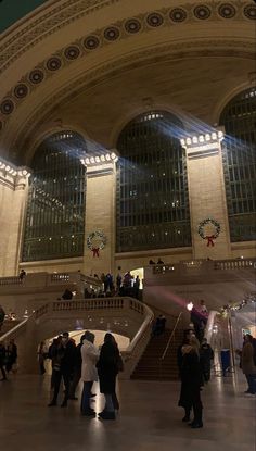 many people are standing in the lobby of a train station at night with their lights on