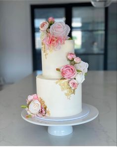 a three tiered cake with pink and white flowers on the top is sitting on a plate