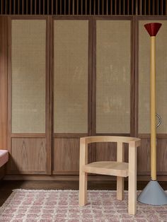 a wooden chair sitting next to a lamp on top of a rug in front of a wall