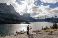 a bride and groom standing on the edge of a mountain overlooking a lake