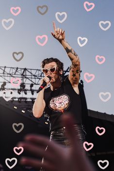 a man in black shirt and sunglasses on stage with heart shaped confetti around him