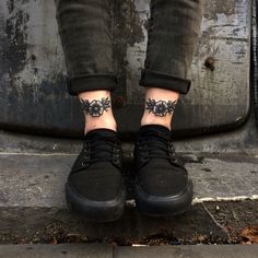 a person with a tattoo on their left foot wearing black sneakers and jeans, standing in front of a metal door