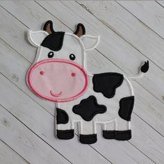 a black and white cow with pink nose on a wooden floor next to wood planks